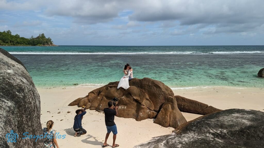 Az esküvői fotózáson a pár Baie Lazare egyik tenger közeli szikláján áll miközben képek készülnek róluk.