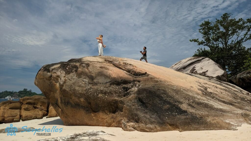 Az esküvői fotózáson felvételek készülnek az ifjú párról Baie Lazare hatalmas parti szikláján állva.