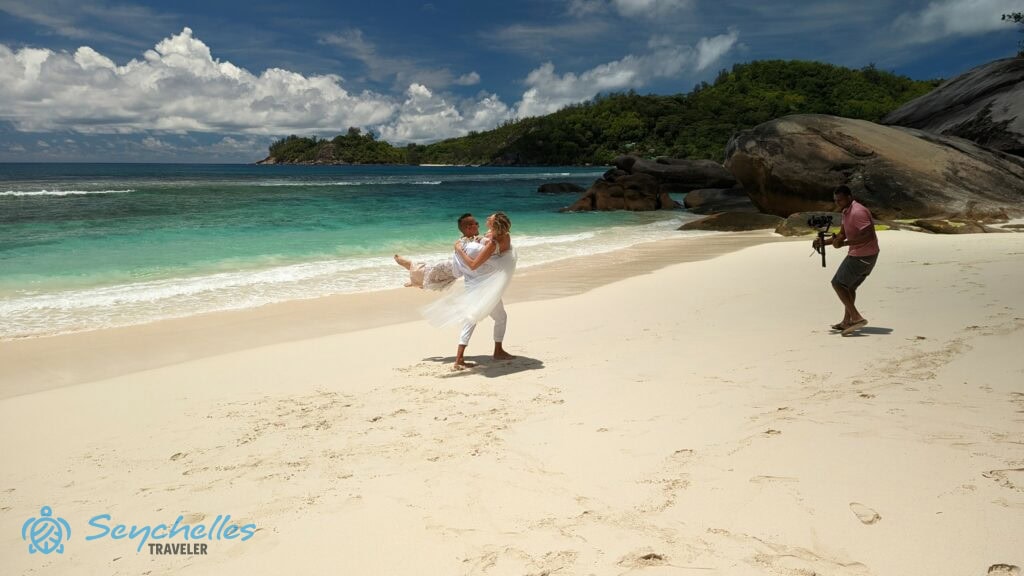 A vőlegény a karjában tartja a menyasszonyt és úgy sétál vele az esküvői videózáson Baie Lazare parton.