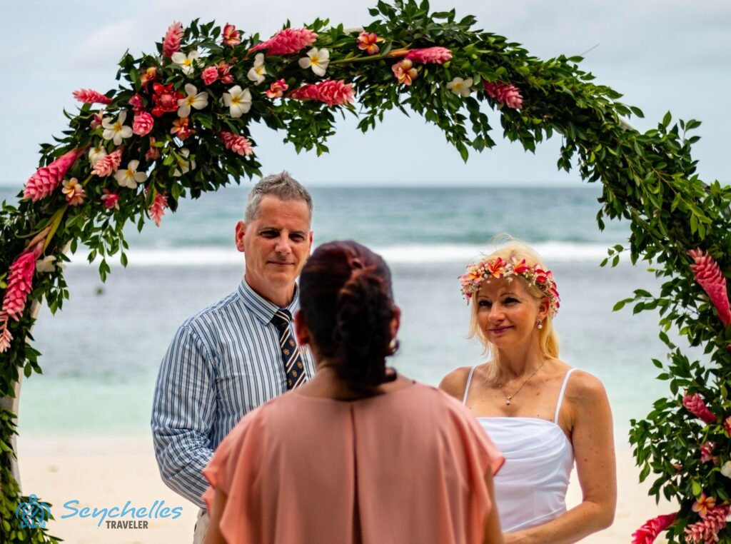 A jegyespár gyűrű formájú, virágos boldogságkapuban állva figyeli az anyakönyvvezetőt az angol nyelvű hivatalos esküvőn.