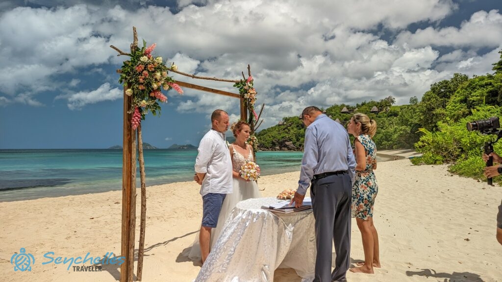 Anse Louis parton, a virágokkal díszített kapu alatt álló pár Rékát hallgatja a magyar nyelvű hivatalos esküvőn.