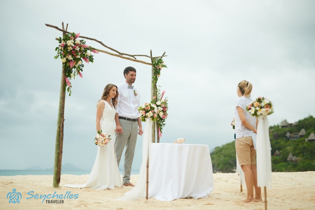 Fiatal pár hallgatja a köszöntő beszédet magyar nyelvű szimbolikus esküvőjükön, Anse Louis tengerparton.