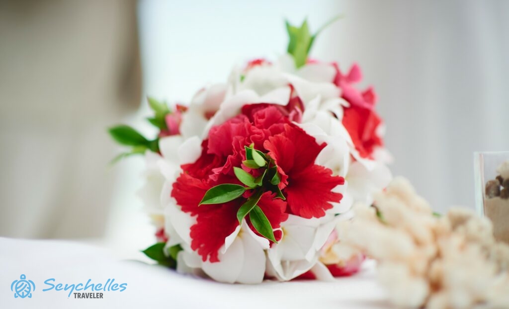 Fehér frangipániból és piros hibiszkuszból készült menyasszonyi csokor pihen az asztalon, La Digue-en.