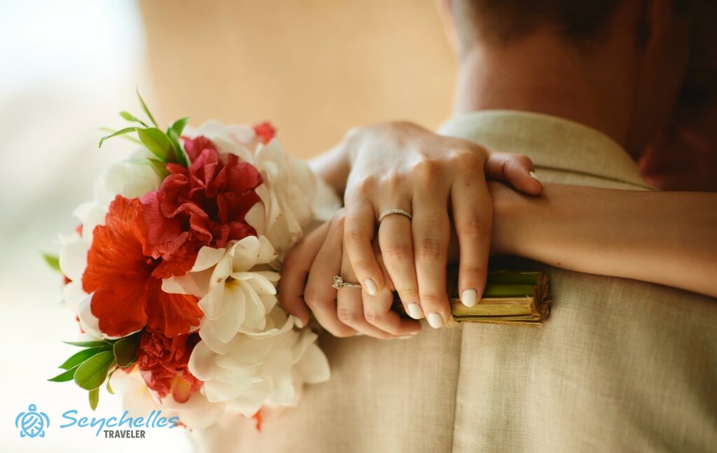 A menyasszony átöleli a vőlegény nyakát, kezében a fehér frangipániból és piros hibiszkuszból álló menyasszonyi csokorral.