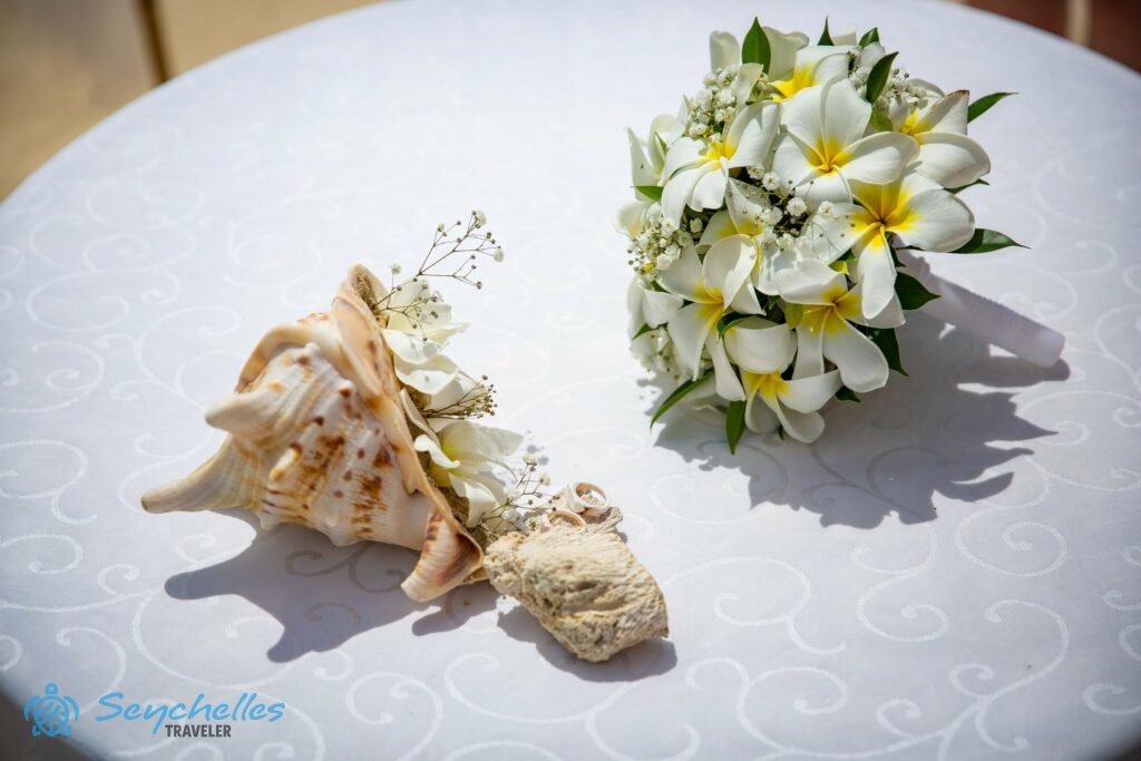 Sárga közepű, nagyobb frangipáni virágokból, rezgőből és zöld levelekből álló menyasszonyi csokor az asztalon, Mahén.