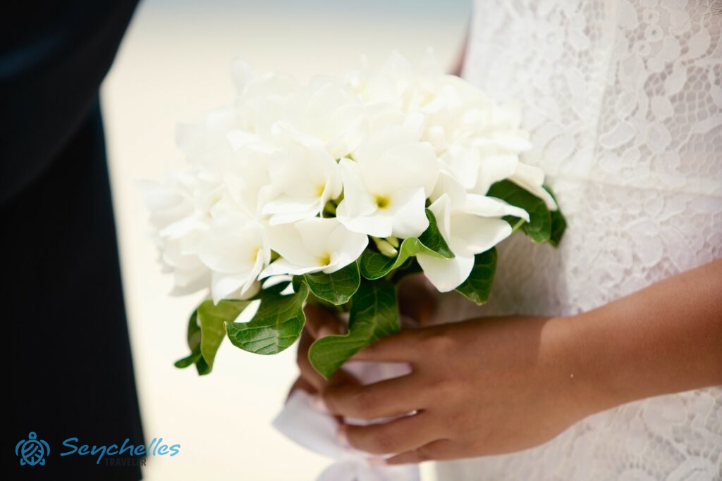 Közeli kép egy hófehér virágokból álló, alulról zöld levelekkel díszített menyasszonyi csokorról.