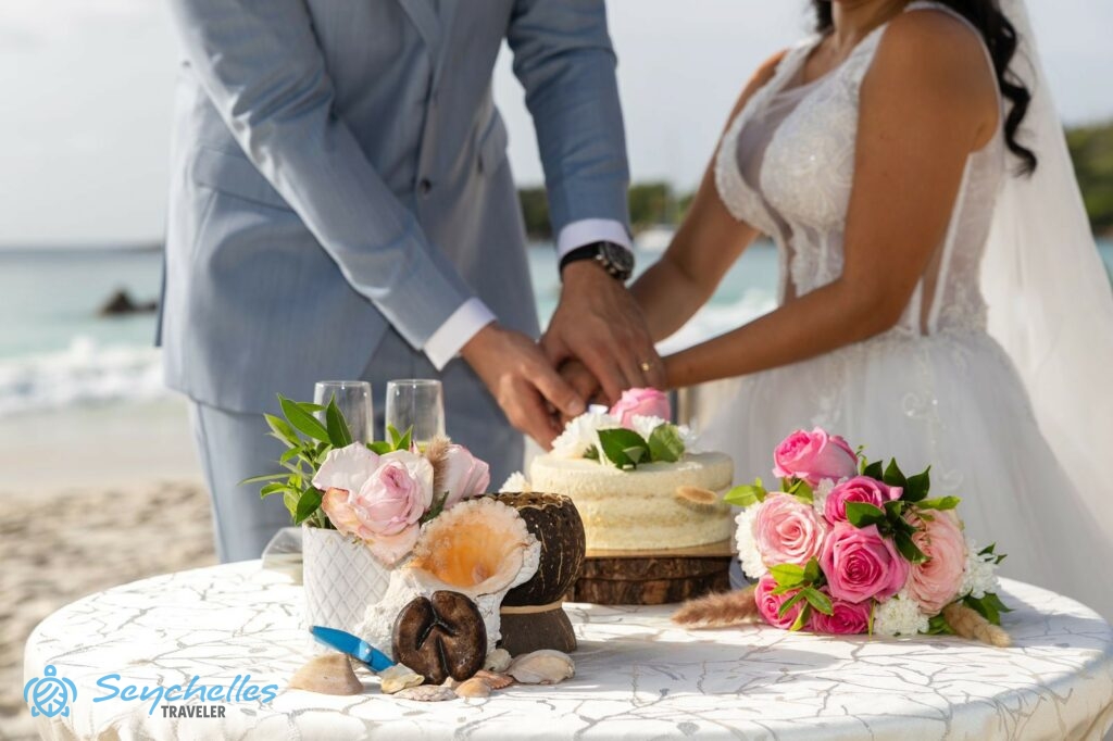 Az ifjú pár az esküvői tortát vágja fel, amely mellett asztaldísz és rózsaszín rózsákból készült menyasszonyi csokor.