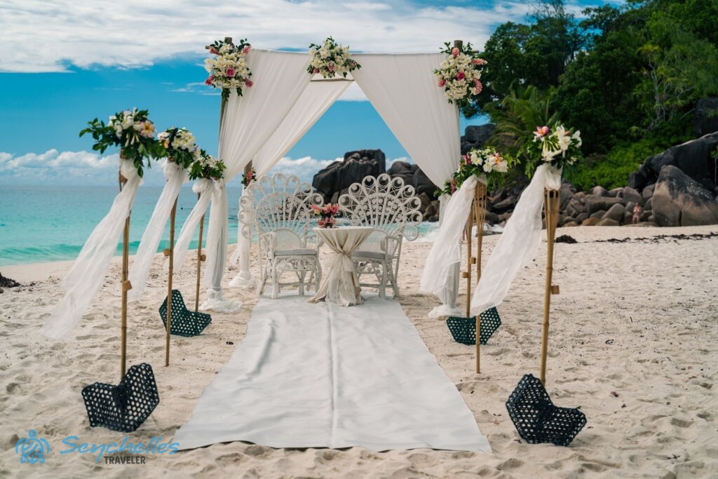 Fehér szőnyeggel takart, 6 oszloppal díszített bevonuló folyosó, esküvői asztal pávaszékekkel a pavilon alatt.