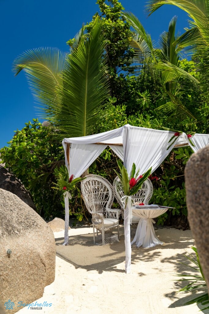 Árnyékot adó esküvői pavilon a trópusi növényzet mellett La Digue-en a tengerparti homokban, gránitsziklák közelében.