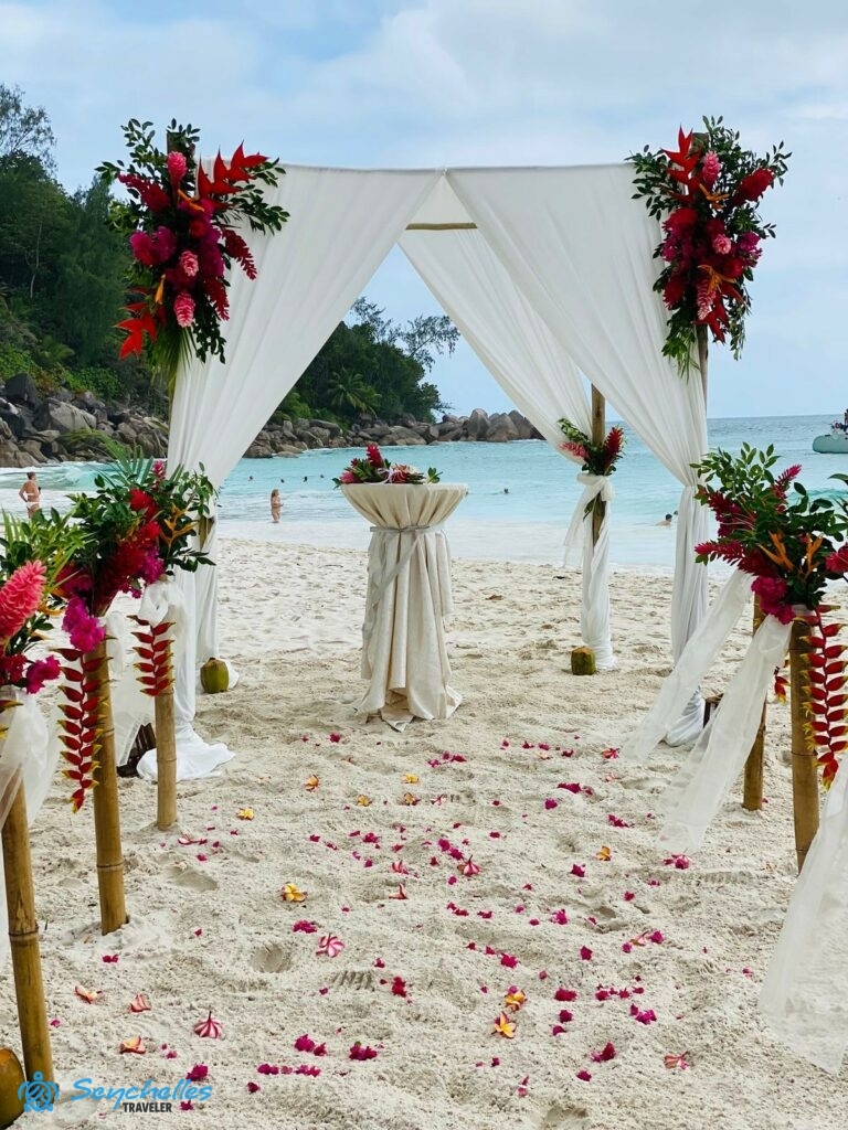 Rózsaszín és piros árnyalatú virágokkal díszített bevonuló folyosó és esküvői pavilon a tengerparton Praslin-en.