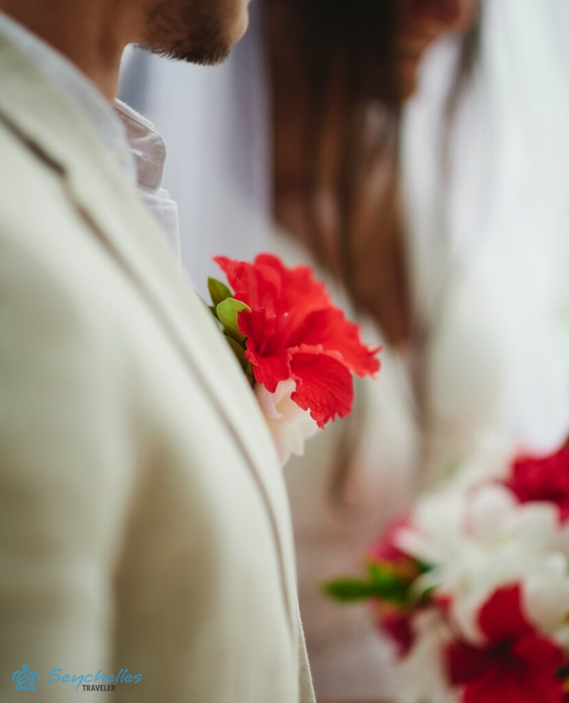 Piros hibiszkusz virágból készült gomblyukdísz a vőlegényen.