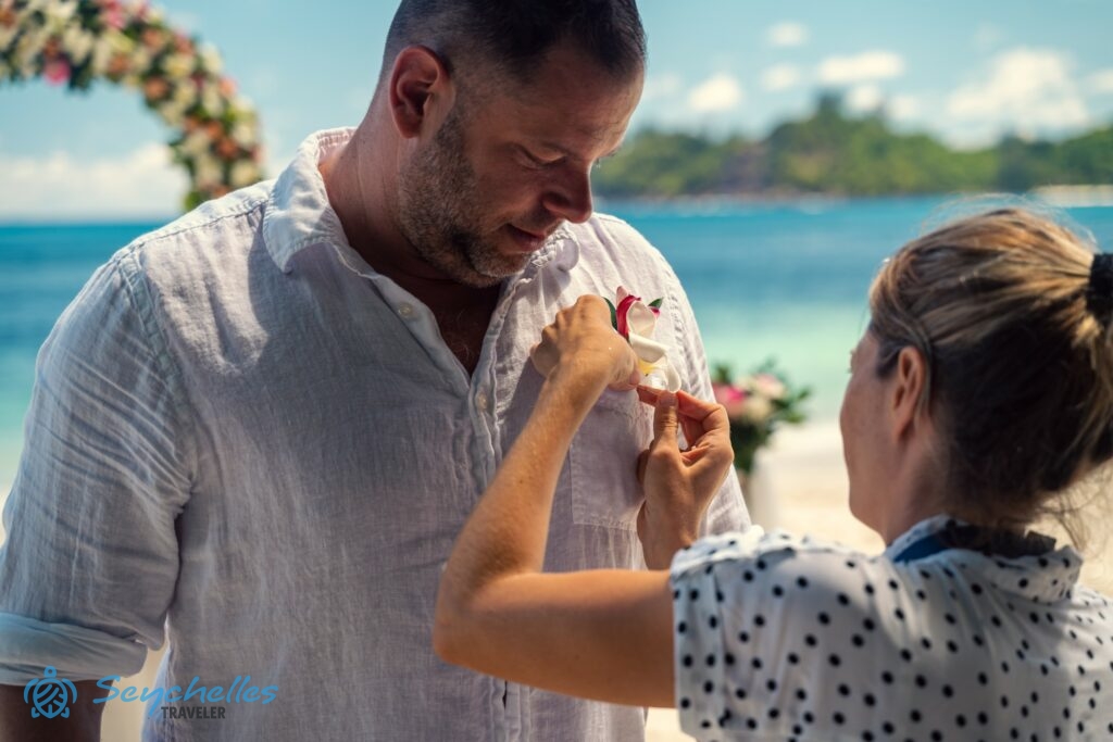 Réka a trópusi virágból készült gomblyukdíszt elhelyezi a vőlegény ingjén Mahén.