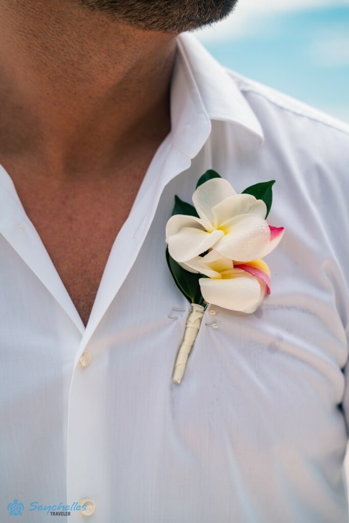 Közeli kép a vőlegény ingén lévő, frangipániból készült gomblyukdíszről.