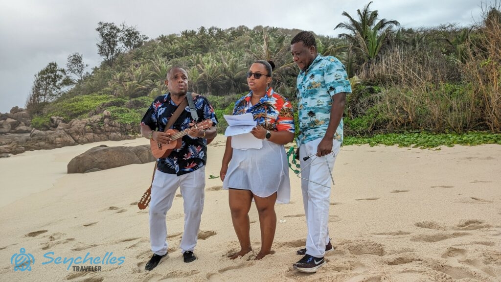 Zenészek állnak különböző hangszerekkel a kezükben Anse Bazarca tengerparton.