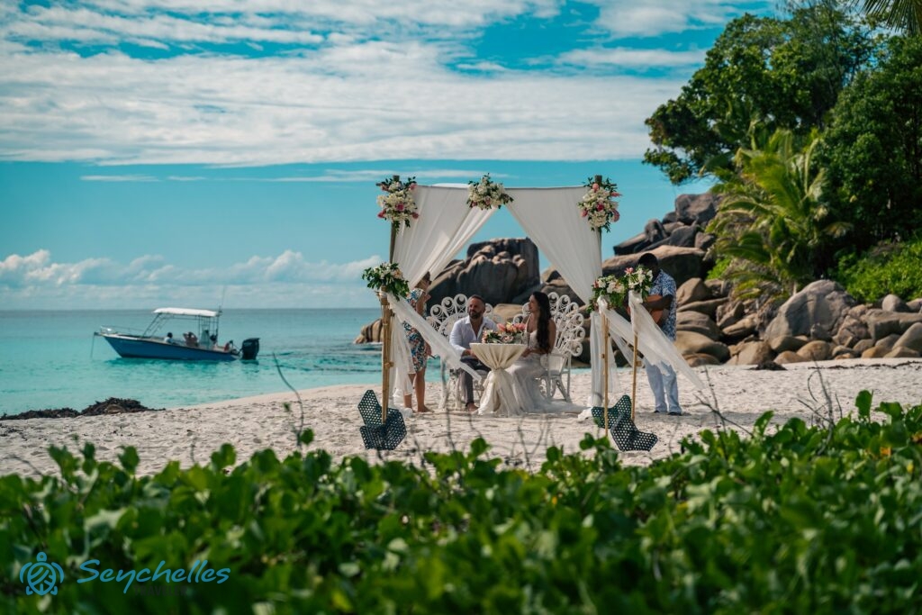 Feldíszített esküvői helyszín a friss házasokkal, Rékával és egy zenésszel Anse Georgette tengerparton.