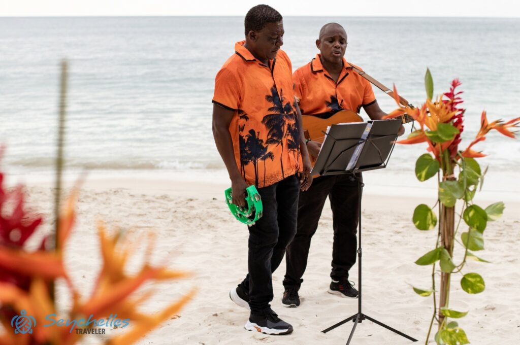Színes inges zenészek a filodendronnal, gyömbér és papagájvirágokkal díszített esküvői dekoráció mögött, Anse Louis parton.