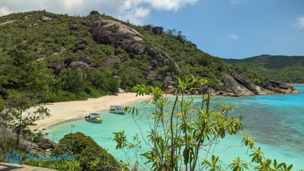 Anse Du Riz fehér homokos öble és gránitsziklái egy északi oldalon lévő magaslatról fényképezve.