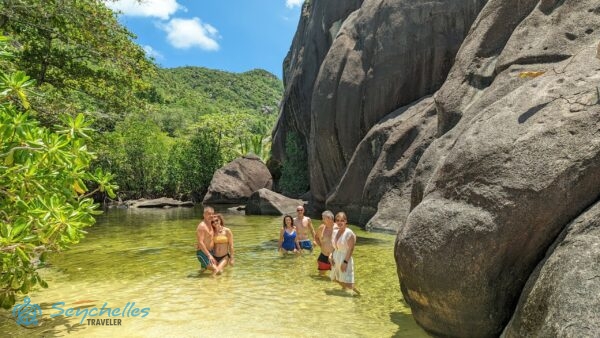 Látogatók állnak a gránit sziklák tövében kialakult természetes édesvizes medencében Anse Du Riz partnál.