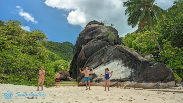 Látogatók állnak a homokban Anse Du Riz parton a gránitsziklák és az édesvizű tó előtt.