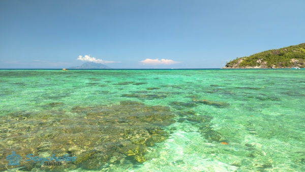 Korallblokkokkal tűzdelt, átlátszó, sekély tenger Baie Ternay Tengeri Nemzeti Parkban, a távolban Silhouette-szigettel.