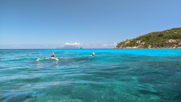 Sznorkelezők úsznak Baie Ternay Tengeri Nemzeti Parkban, a vízben őrmester halakkal, a háttérben Silhouette-sziget látszódik.