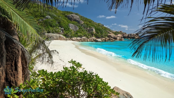 Enyhén hullámzó kristálytiszta óceán Grande Soeur keleti, fehér homokos partjánál gránitsziklákkal.