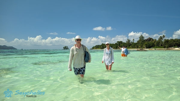 Vidám látogatók sétálnak az átlátszó vízben Anse Source d'Argent partnál.