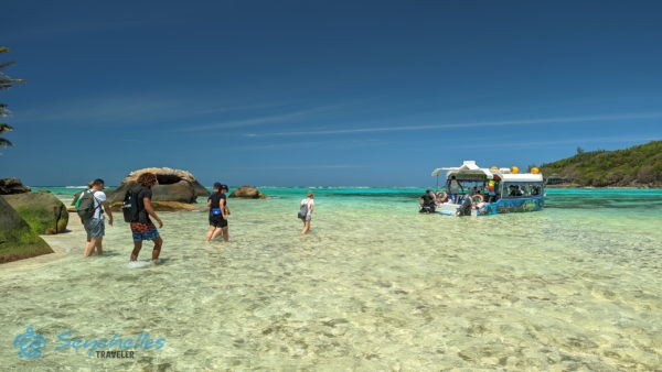 Réka és a vendégek a sekély vízben az üvegfenekű hajó felé sétálnak Moyenne-szigetnél.