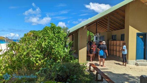 Vendégek sétálnak a növényzettel körbevett látogatóközpontban a homokon.