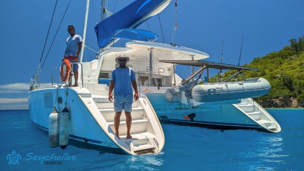 A kapitány az Endless katamarán lépcsőjén áll, a legénység másik tagja a hajó oldaláról figyeli a tengert.