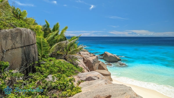 Egy szikla tetejéről készített kép Grande Soeur keleti partjának gránit tömbjeiről, a dús vegetációról és a tengerről.