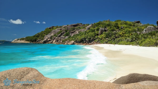 Grande Soeur fehér homokos tengerpartja fürdőző látogatókkal és a keleti oldal sziklákkal tűzdelt zöld dombjai.