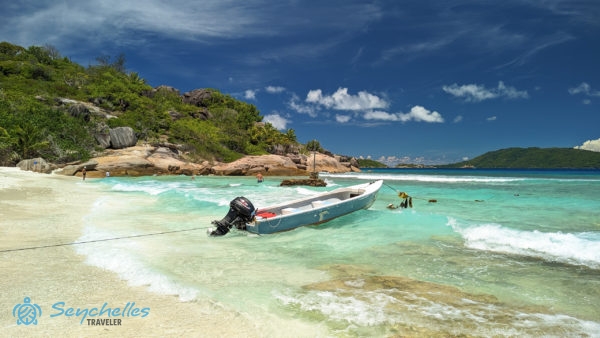 Grande Soeur enyhén hullámos nyugati partja csónakkal, vízben fürdőző látogatókkal és a partszakasz végén gránitsziklákkal.