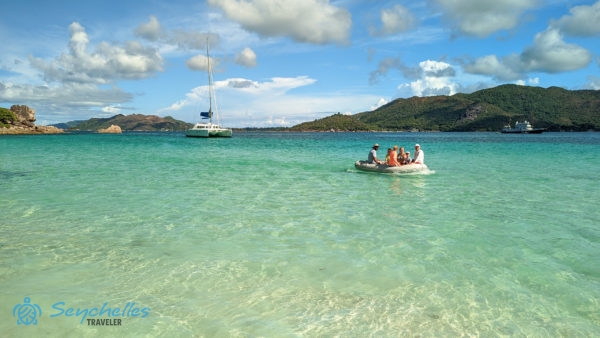 A kis motorcsónak a látogatókkal a sekély vízbe ér, a háttérben a katamarán látszódik.